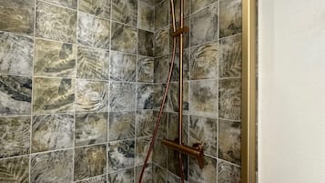 A shower with a handheld showerhead and a rain shower head, surrounded by marble-patterned tiles.
