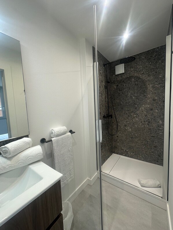 Un baño moderno con cabina de ducha de vidrio, azulejos blancos y una pared con textura de mármol.