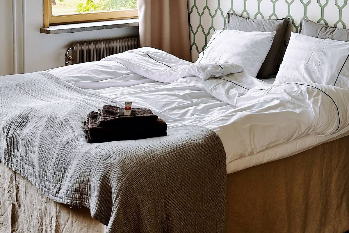 Un dormitorio con cama, ventana con cortinas, radiador y pared con diseño.