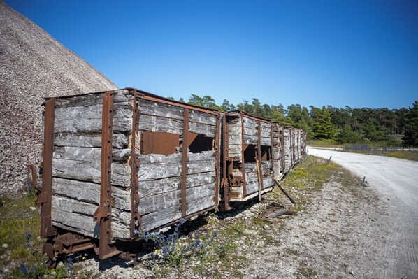 A dilapidated wooden structure with metal supports, located beside a gravel road with a forest in the background. - Bungenäs Badhotell (Fårösund)