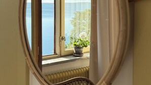 A room with a large oval mirror reflecting a window view of the sea and a potted plant on the windowsill. - Bungenäs Badhotell (Fårösund)