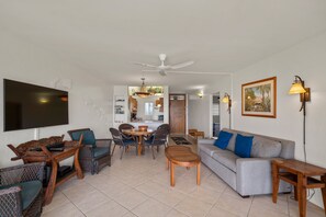 A living room with a flat-screen TV, wicker furniture, a grey sofa, and a ceiling fan. - Menehune Shores, #118^ 3 Bedroom Condo (Kihei)