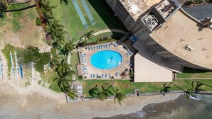 An aerial view of a resort with a central swimming pool, beach area, and adjacent hotel buildings. - Menehune Shores, #118^ 3 Bedroom Condo (Kihei)