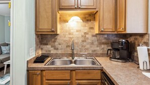 Una cocina con gabinetes de madera, un lavamanos doble, una cafetera y un salpicadero de azulejos.