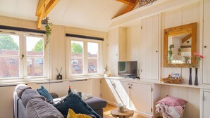 A cozy living room with a sofa, a small table, and a kitchen area with a TV and wooden cabinets. - Pat's Home, sleeping under the stars. (Alkmaar)