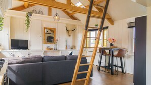 A modern kitchen with a wooden ceiling, a large gray sofa, and a dining area with two chairs. - Pat's Home, sleeping under the stars. (Alkmaar)