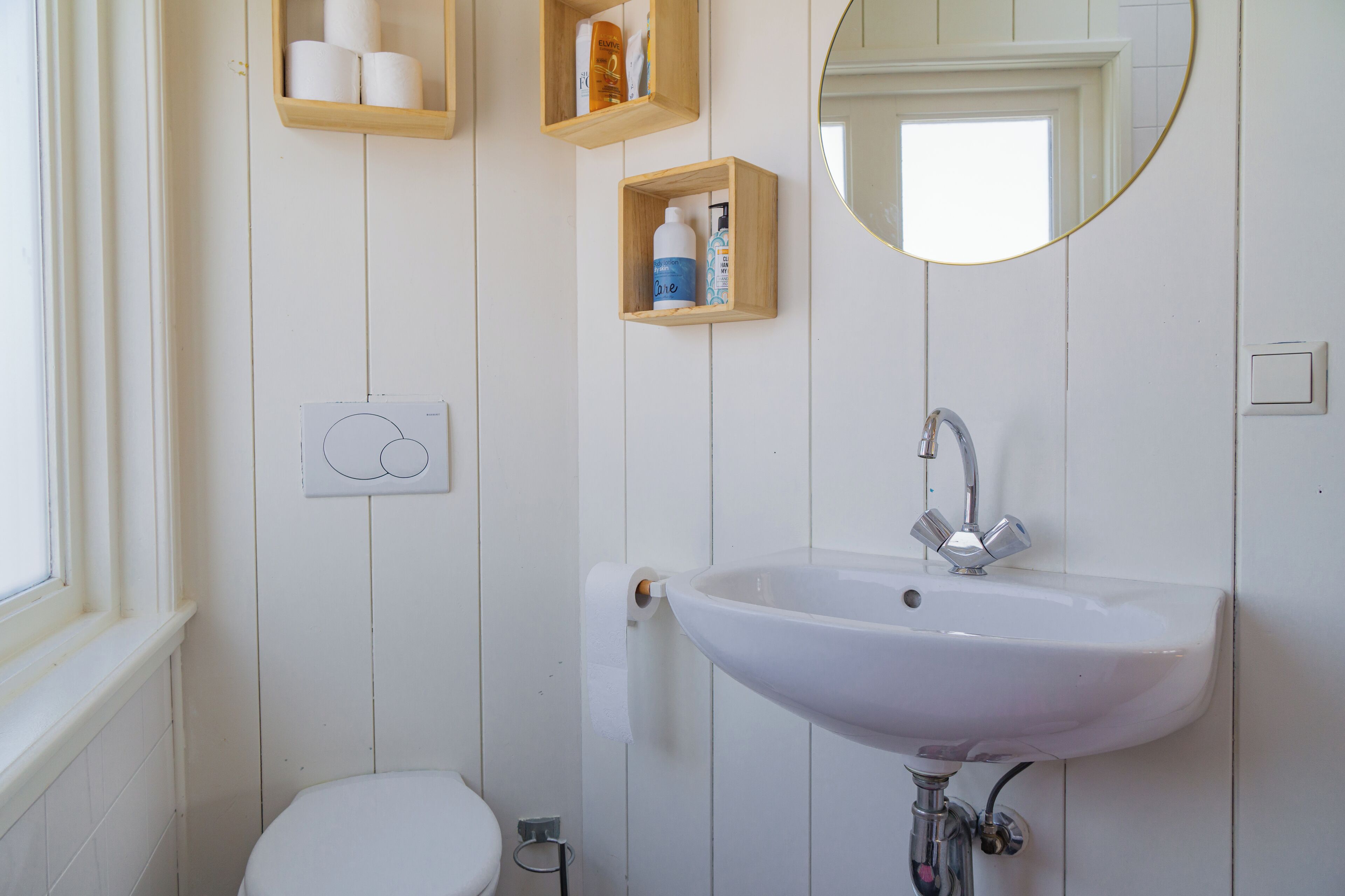 A bathroom with a white sink, toilet, and wooden shelves with toiletries.