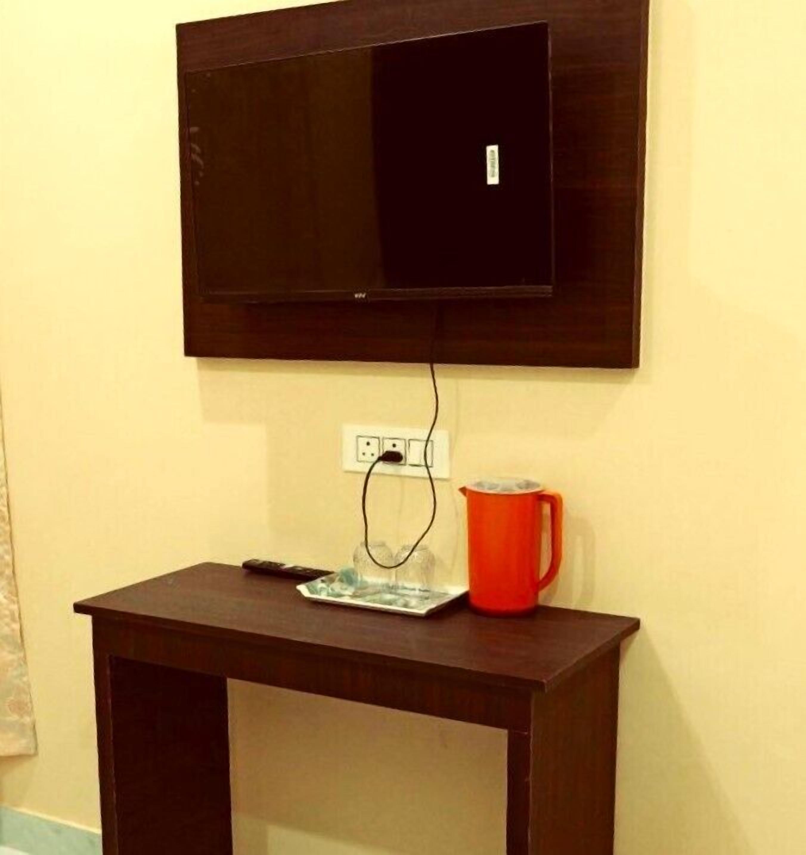 A TV mounted on a wall above a wooden table with a remote control, a glass, and a red mug on it.