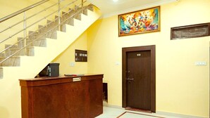 A reception desk with a sign, a staircase, a door, and a wall with a painting. - Hotel The Ram Krishna (Rajnagar)