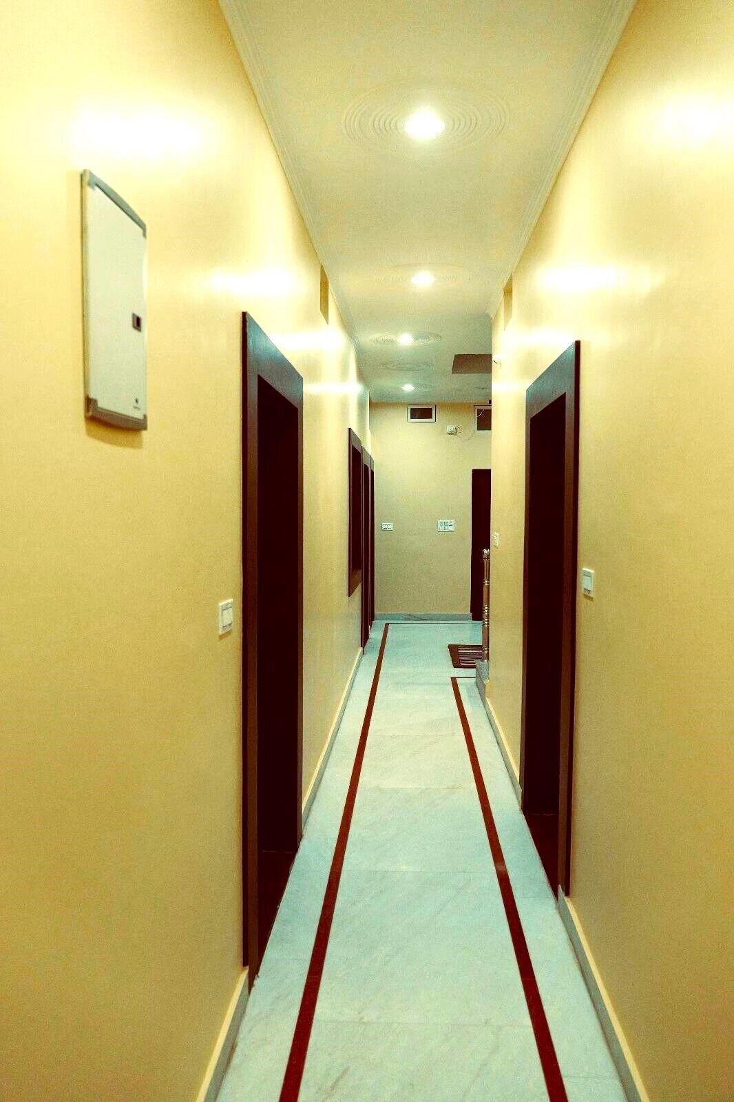 A hotel hallway with a light blue carpet and red stripes, leading to a door at the end.
