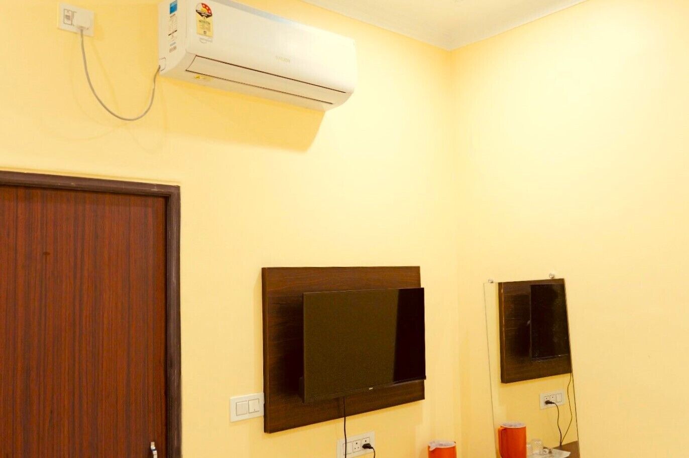 A room with a wooden door, a mounted air conditioner, and two wall-mounted televisions.