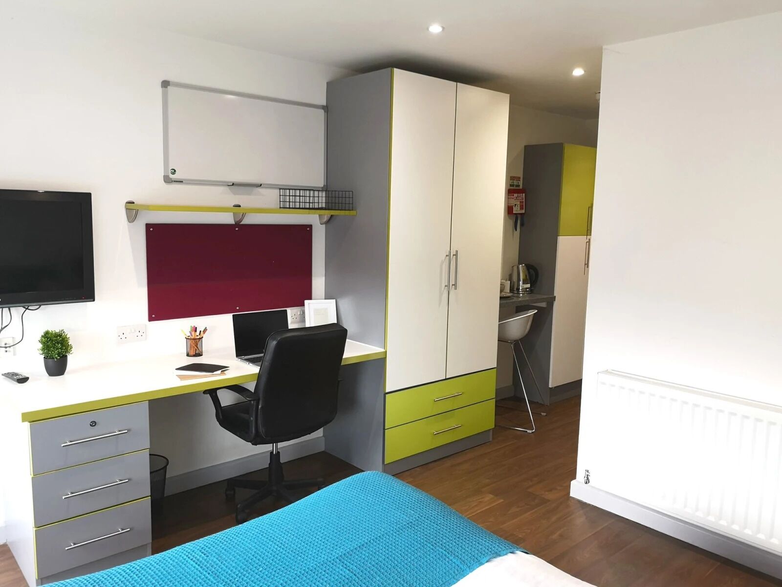 A compact bedroom with a bed, a desk with a chair, a TV, and a wardrobe.