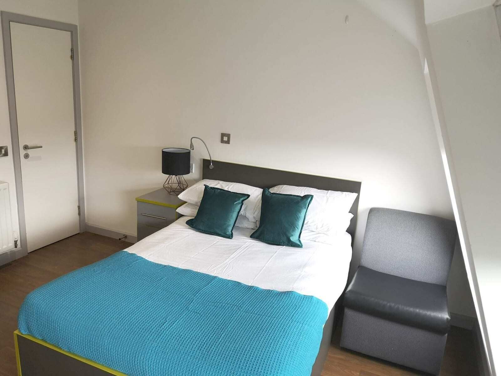 A bedroom with a bed, a nightstand, a lamp, and a chair.