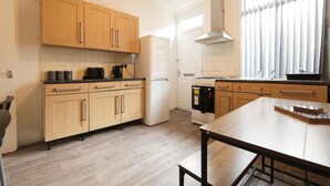 A modern kitchen with wooden cabinets, a built-in oven, and a window with curtains. - House-sleeps8-parking-garden (Leeds)