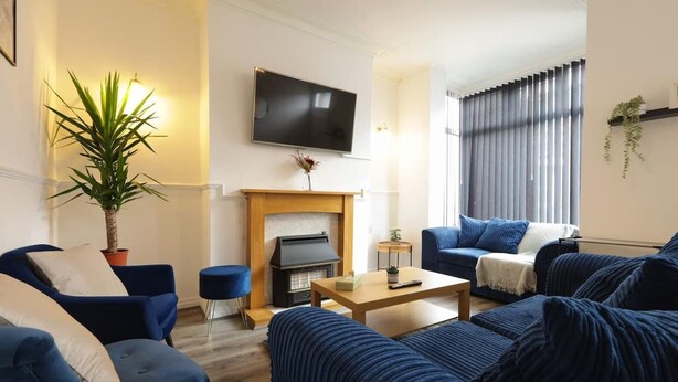 A living room with a fireplace, a television, and blue furniture. - House-sleeps8-parking-garden (Leeds)