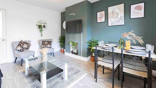 A modern living room with a dining area, featuring a glass coffee table, a sofa, and a TV mounted on the wall. - House-sleeps7-parking-garden-petfriendly (Leeds)