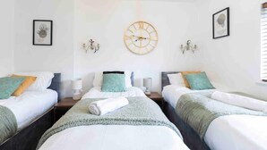 A hotel room with two beds, a large wall clock, and framed artwork. - House-sleeps7-parking-garden-petfriendly (Leeds)