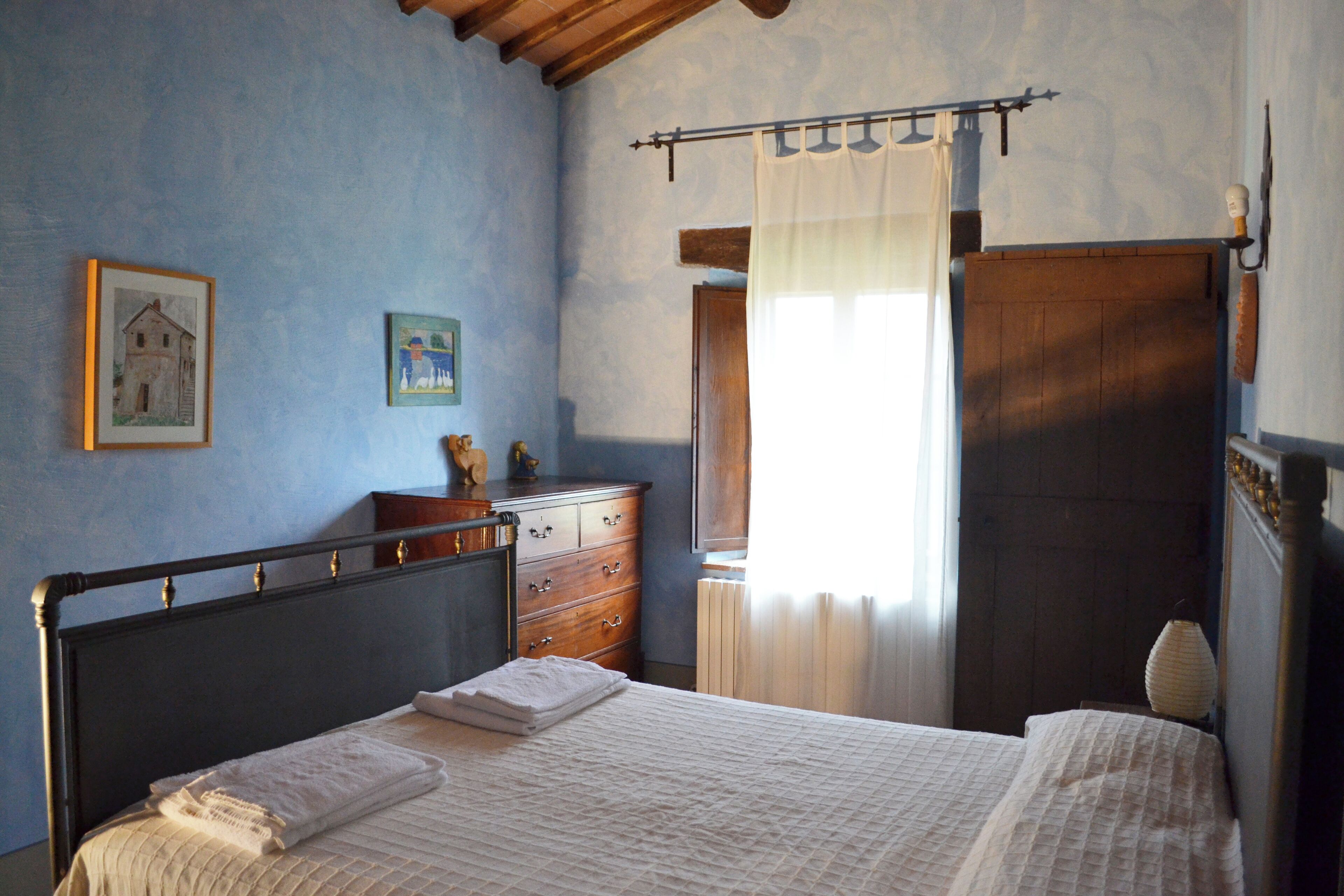 A bedroom with a bed, a dresser, a mirror, and a window with curtains.