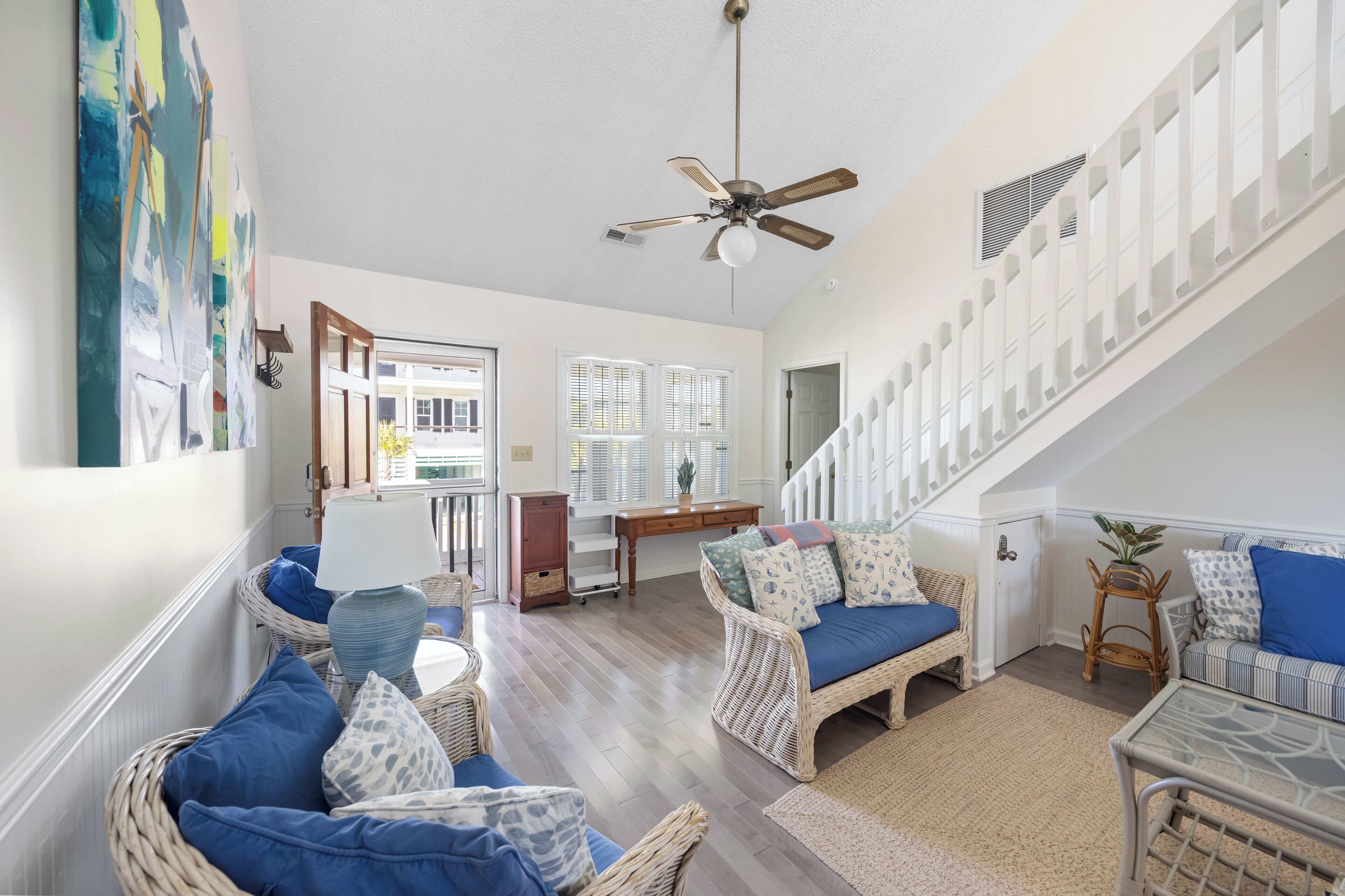 A spacious living room with wicker furniture, a ceiling fan, and a staircase.