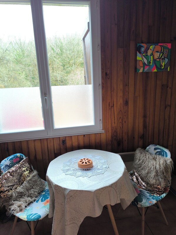 Una habitación con una mesa redonda, dos sillas, un ventanal y un cuadro en la pared.