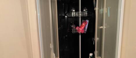 A glass-enclosed shower area with a white base, a small table, and a heater unit.