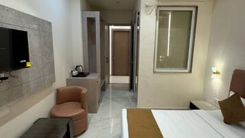A modern hotel room with a bed, a seating area with a chair, a television mounted on the wall, and an air conditioning unit.