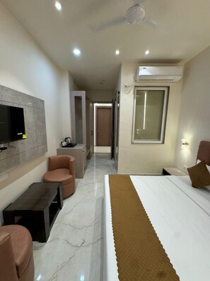 Une chambre d’hôtel moderne équipée d’un lit, d’un coin salon avec un fauteuil, d’un téléviseur fixé au mur et d’un appareil de climatisation.