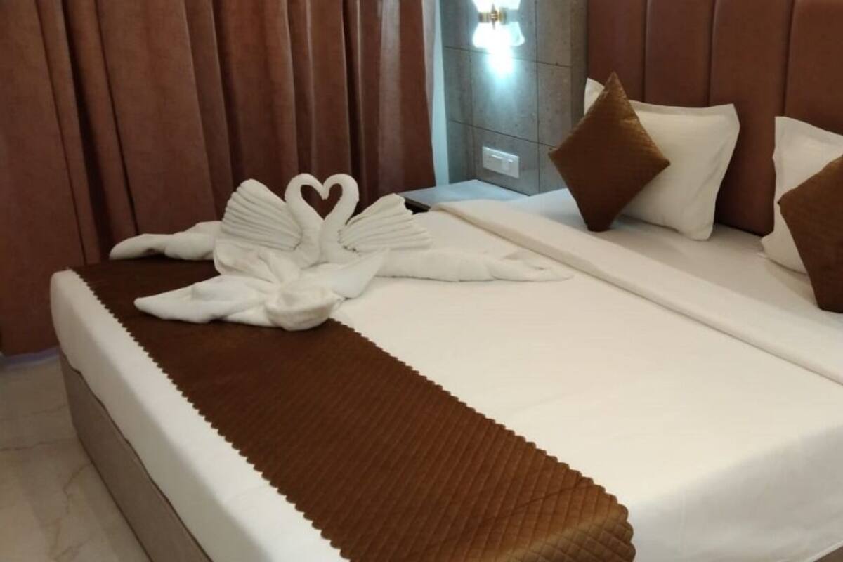 A neatly made bed with a brown throw blanket, white pillows, and a heart-shaped towel arrangement.