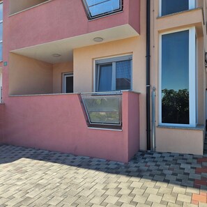 Situated on a paved area, this two-story building features a balcony and upper floor window with metal grills.