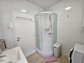 Enjoy a refreshing shower in the corner shower with glass enclosure, adjacent to a modern sink and convenient trash bin.