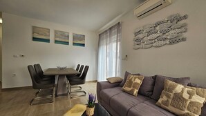 A modern living room with a dining area, featuring a grey sofa, a dining table with chairs, and a decorative wall piece.