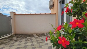 A rooftop terrace with a tiled floor, a beige wall, and red flowers in a pot.