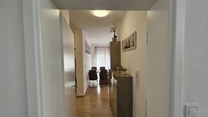A hallway with a dining area at the end, featuring a table and chairs, a cabinet with decorative items, and a light fixture on the ceiling.