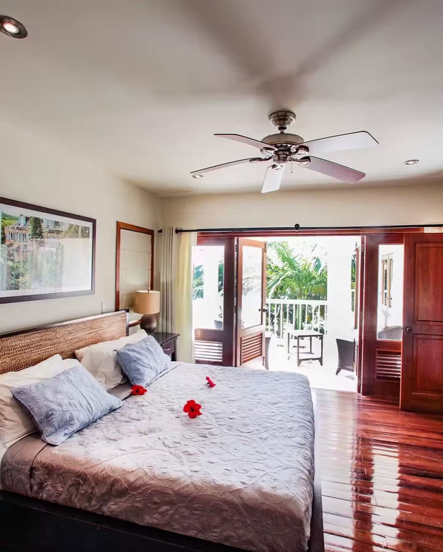 A spacious bedroom with a large bed, a ceiling fan, and a view of a balcony with outdoor furniture.
