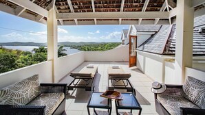 A covered outdoor seating area with lounge chairs and tables, overlooking a scenic landscape.
