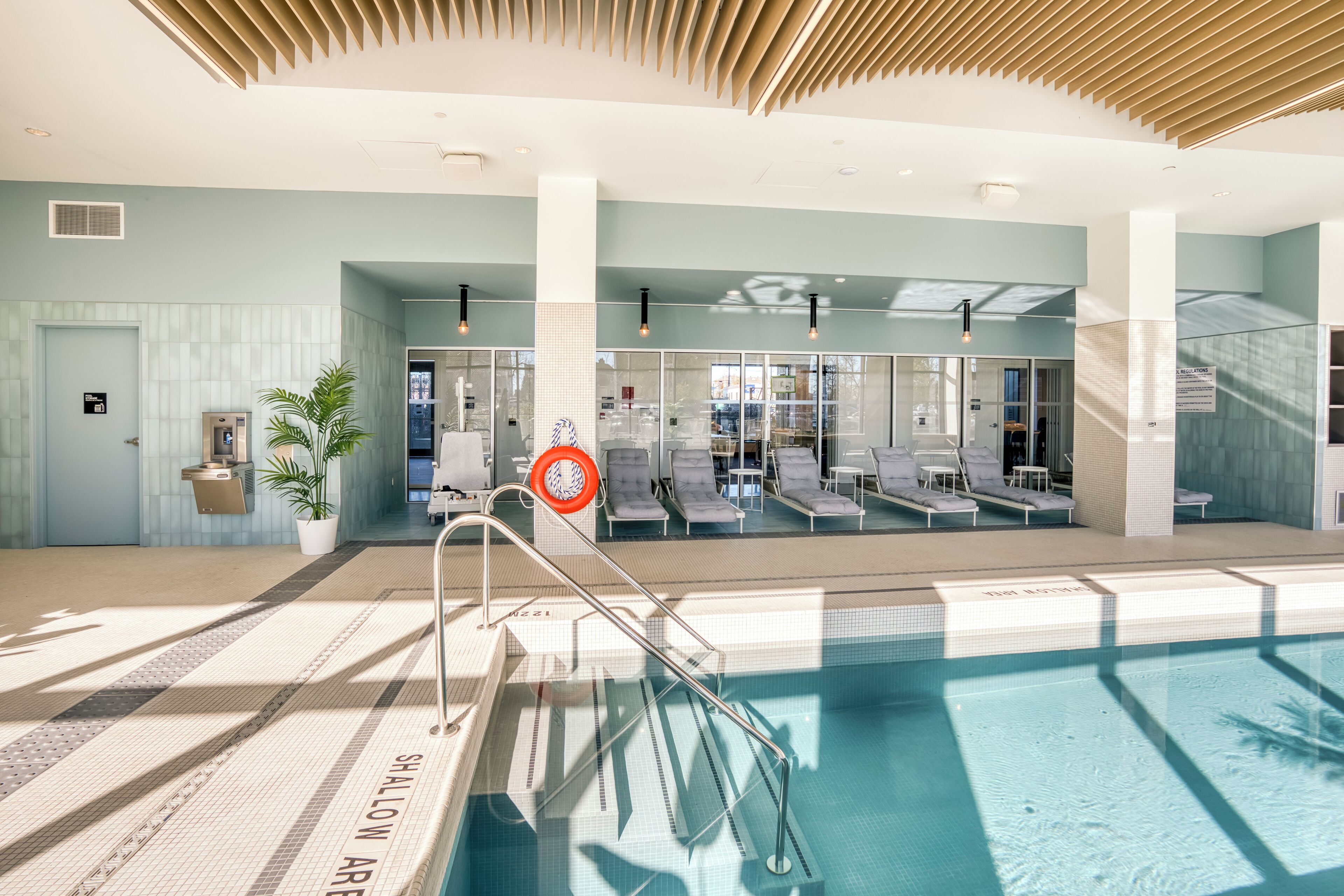 En indendørs swimmingpool med et klart vandareal, liggestole og et solbelyst loft.