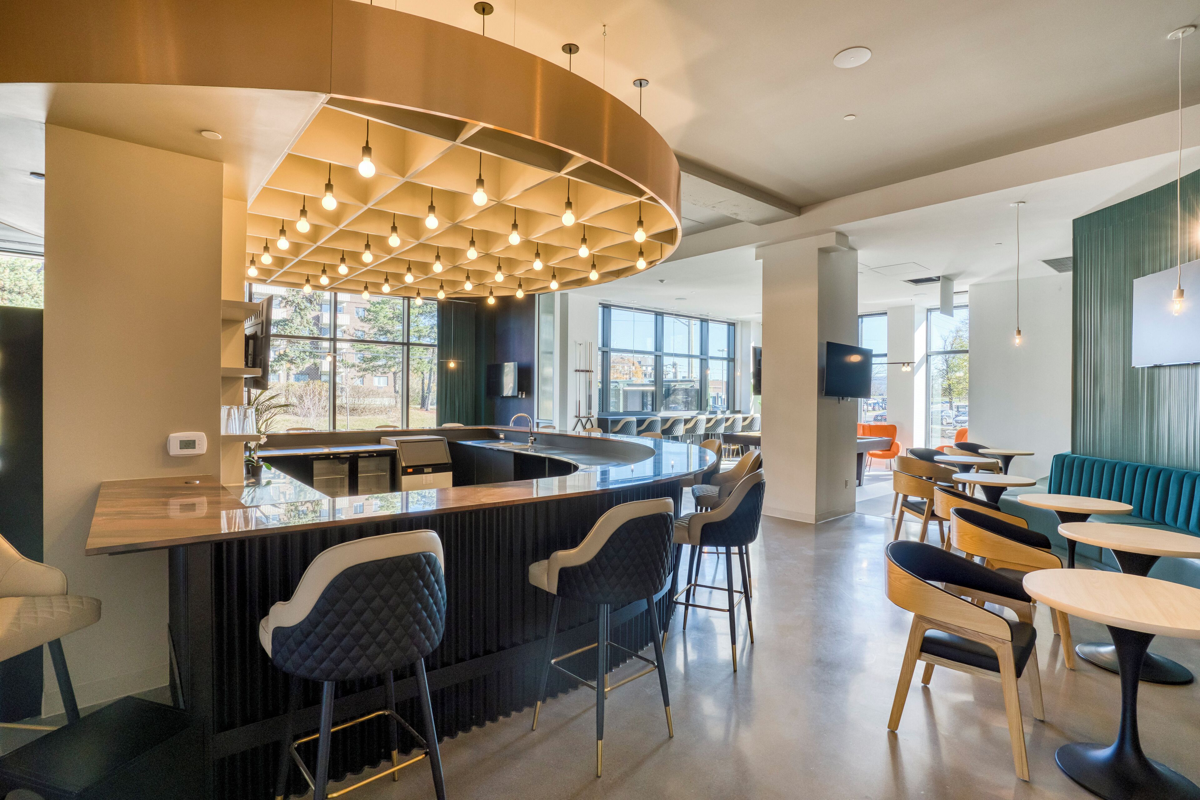 Un espace bar moderne doté d’un comptoir incurvé, de plusieurs tabourets et d’un luminaire suspendu original.