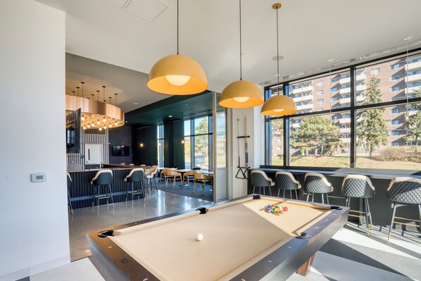 A pool table in a modern indoor setting with large windows, bar seating, and pendant lighting.