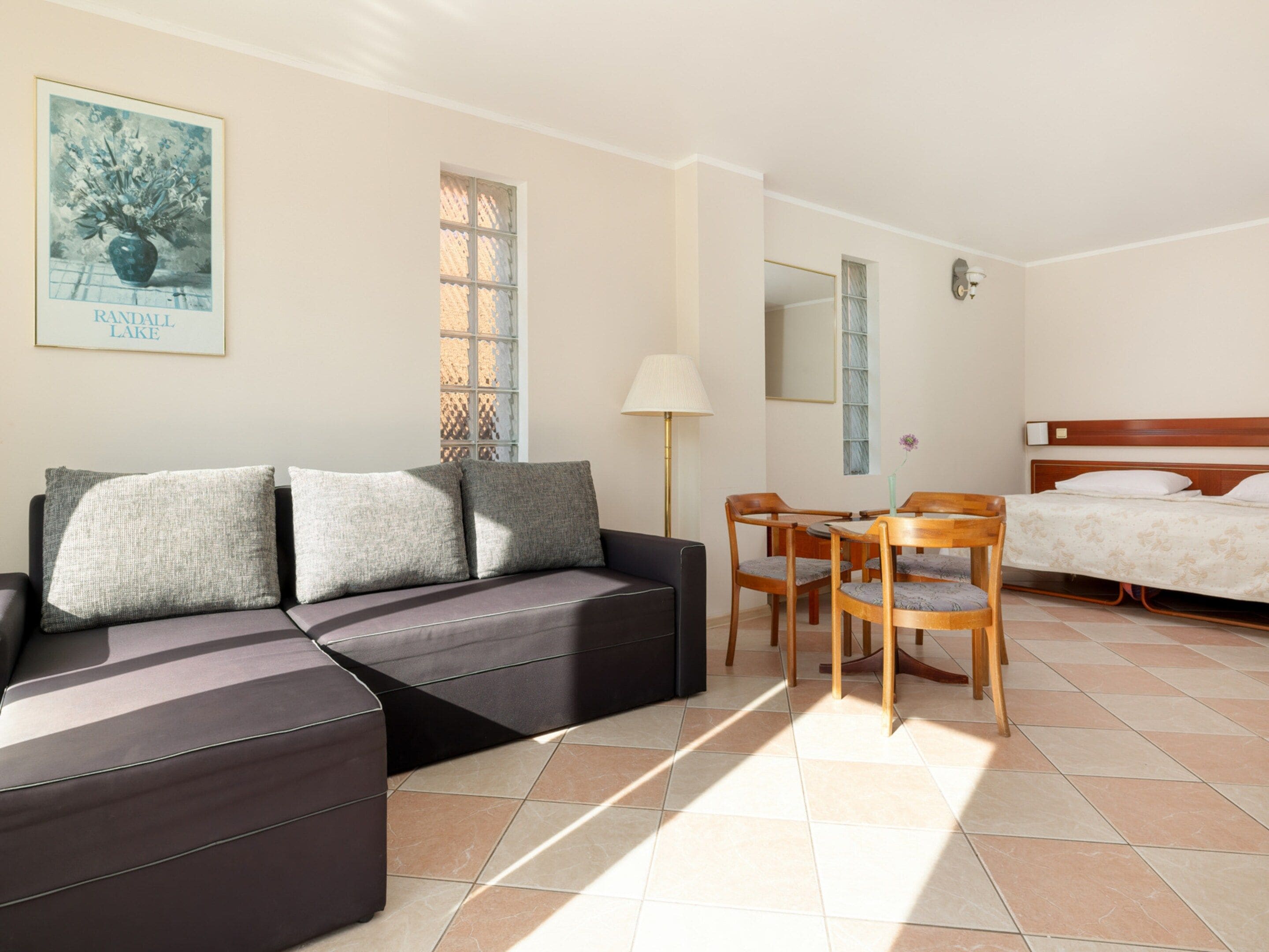 A hotel room with a sofa, a dining table with chairs, a bed, and a window with a view of a tree.