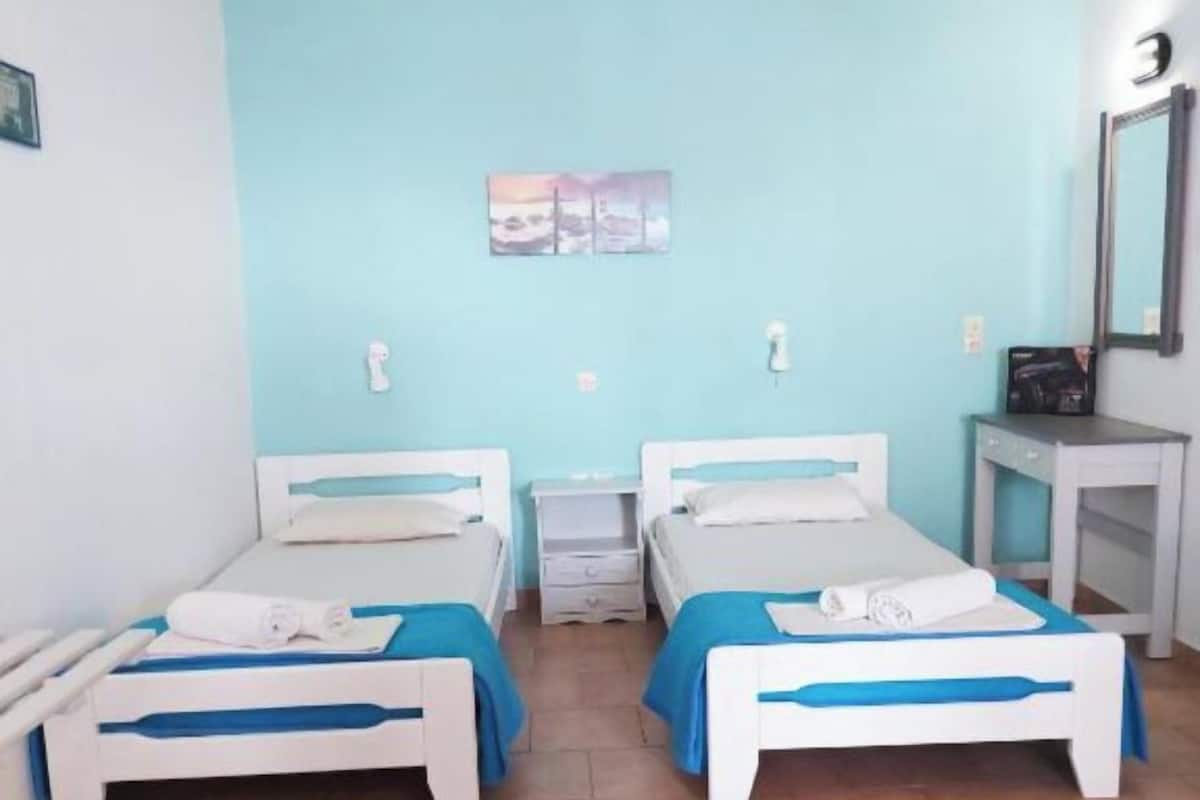 Une chambre avec deux lits, une petite table, un miroir et un tableau accroché au mur.