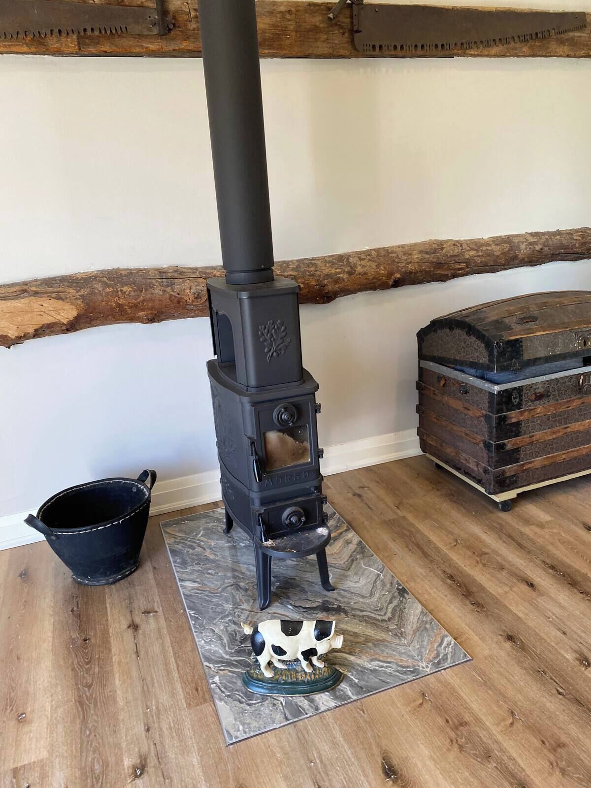 A wood-burning stove with a metal bucket and a decorative cow figurine on a marble-patterned mat.
