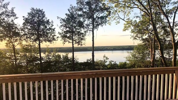 Una terraza de madera con barandilla blanca que da a un lago tranquilo y árboles.