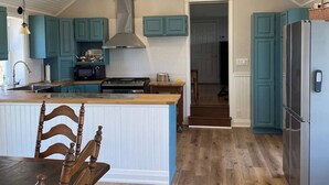 Una cocina con pisos de madera, gabinetes color turquesa, una isla central y un ventilador de techo.
