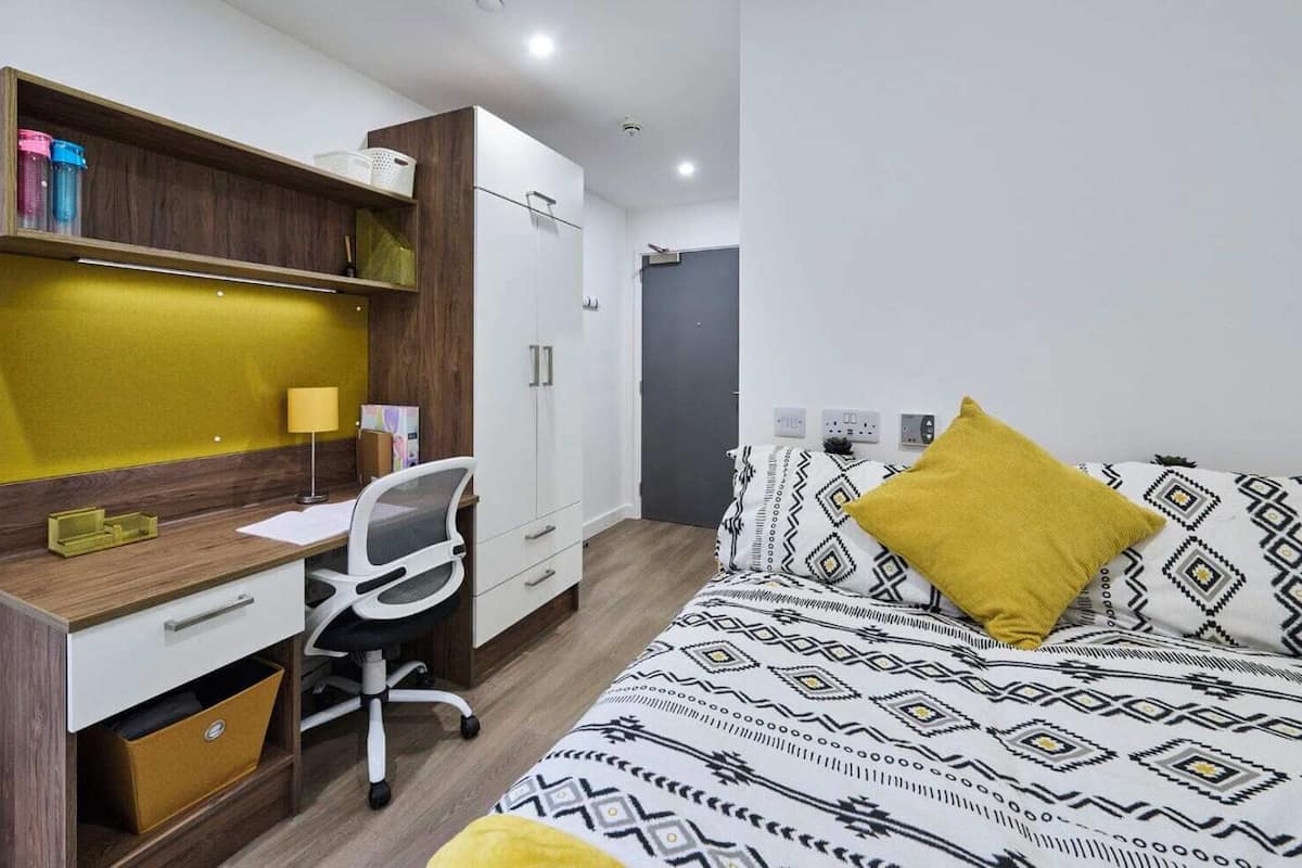 A bedroom with a bed, a desk, and a wardrobe.