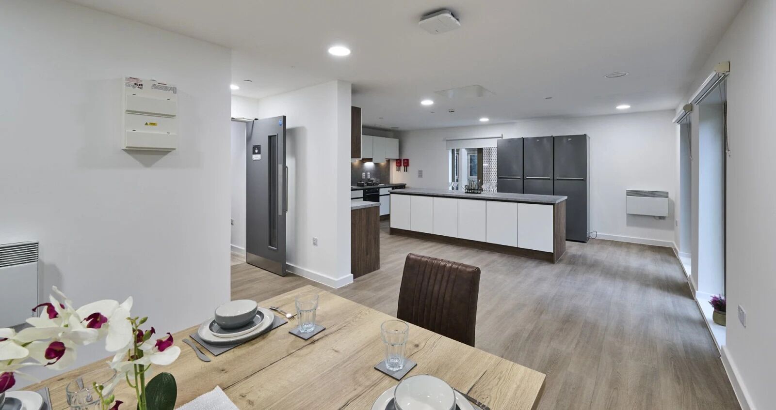 A modern kitchen with stainless steel appliances, a dining area with a wooden table, and a view of the living area.