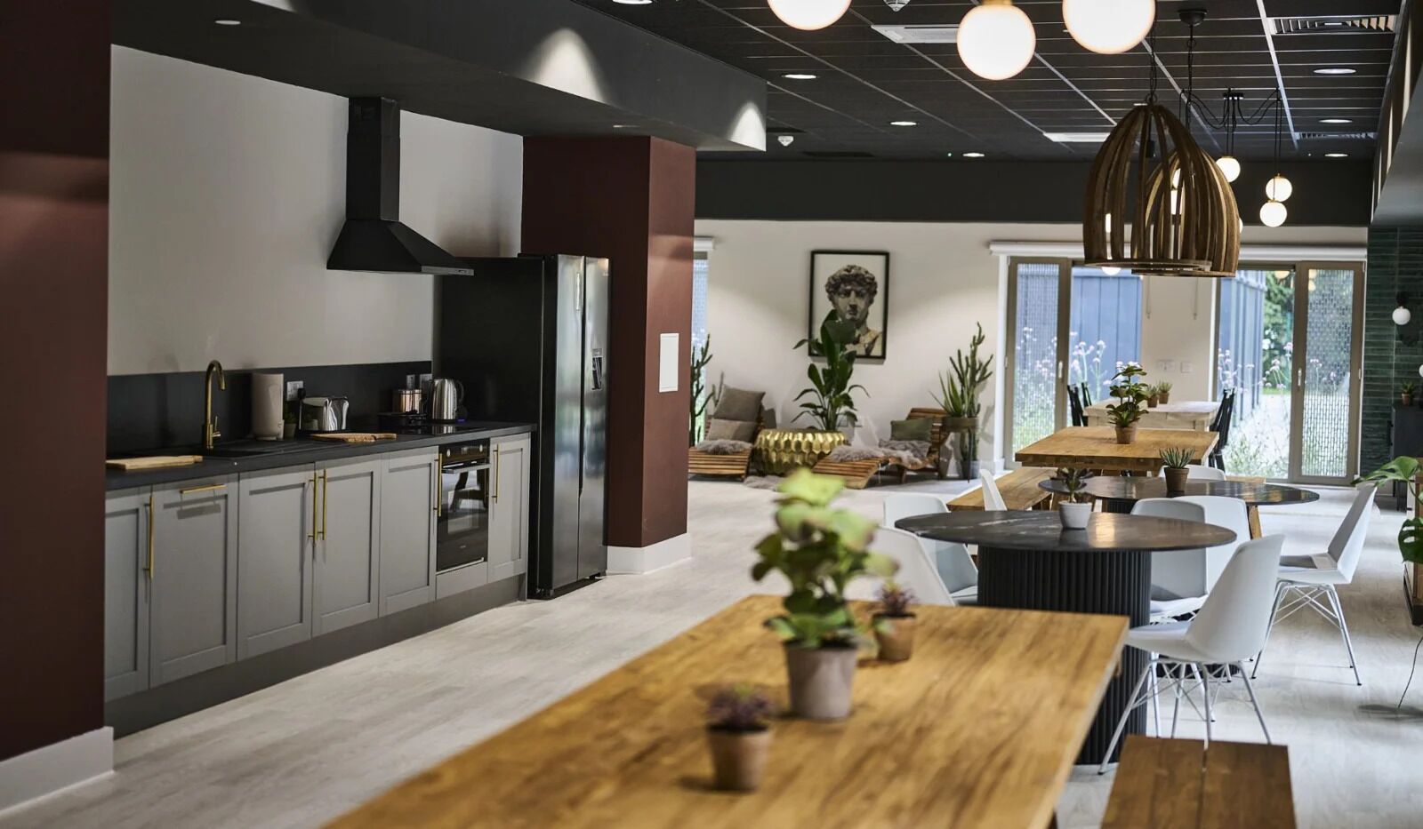 A modern kitchen with grey cabinets, a black refrigerator, and a wooden dining table with chairs.
