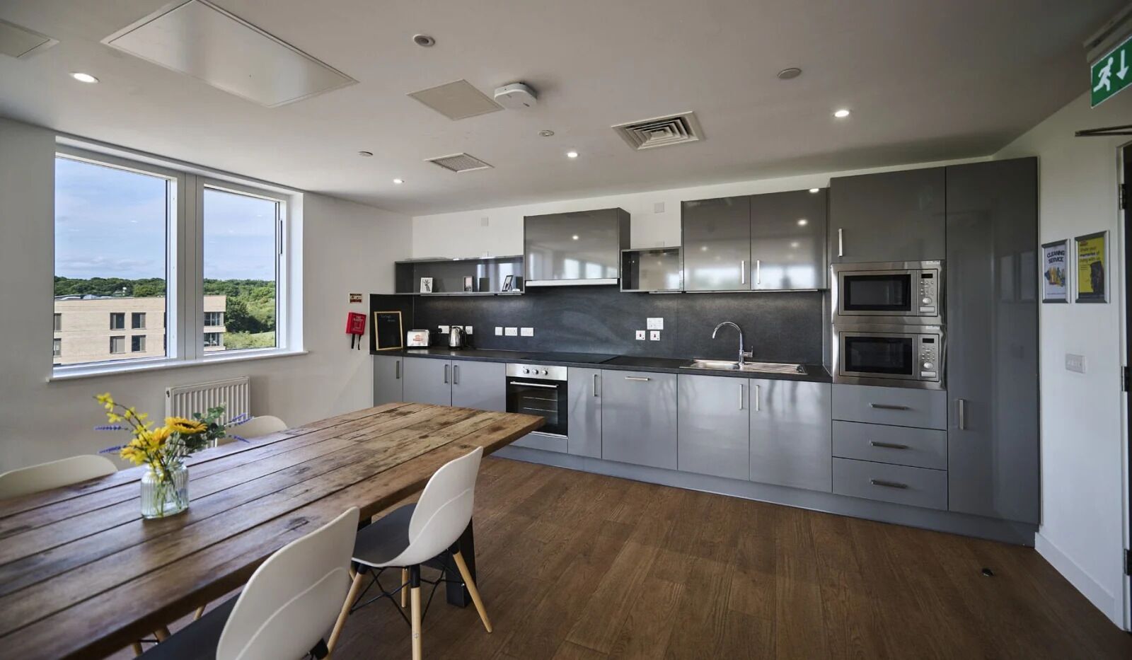 A modern kitchen with stainless steel appliances, a wooden dining table, and a view of buildings outside.