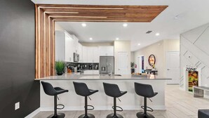 Cozinha moderna com ilha central, banquetas e design de teto em madeira.