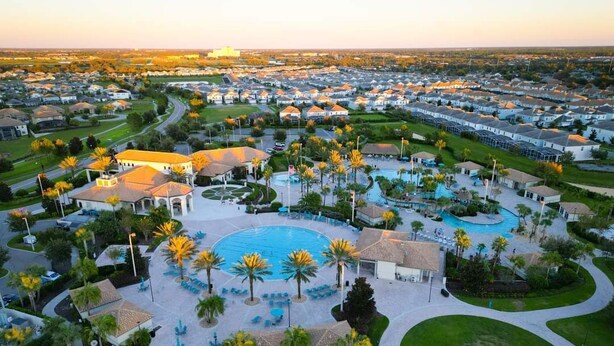 Vista aérea de um bairro residencial com uma piscina central cercada por palmeiras e cadeiras de lounge.