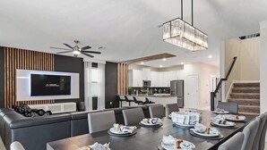 Uma sala de estar moderna com área de jantar, cozinha ao fundo e uma escada.